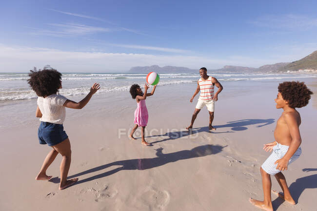 Батьки-афроамериканці і двоє дітей бавляться з м'ячем на пляжі. сім'я на відкритому повітрі відпочиває біля моря. — стокове фото