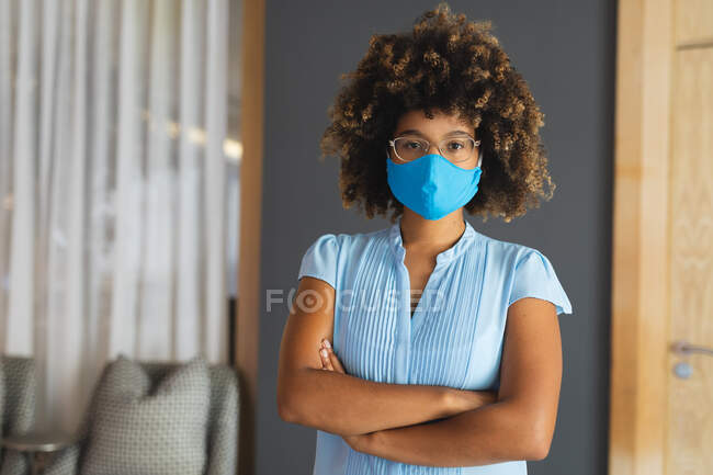 Retrato de mulher de raça mista usando máscara facial em pé no lobby do hotel. hotel de viagens de negócios durante coronavírus covid 19 pandemia. — Fotografia de Stock