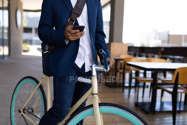 Seção média do macho sentado na bicicleta fora do café usando smartphone. nômade digital, para fora e sobre na cidade. — Fotografia de Stock