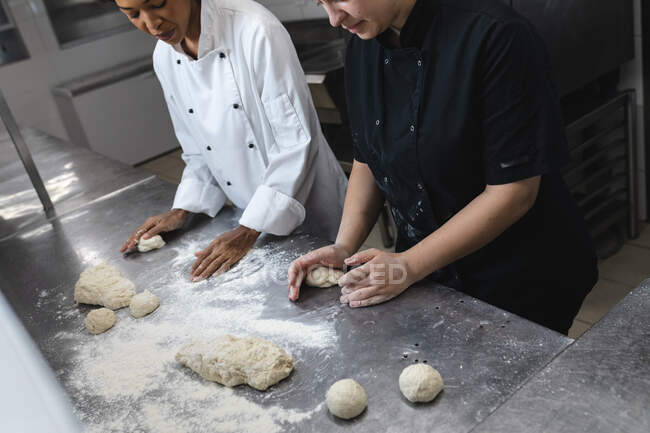 Mixed race professional chefs preparing dough on counter top covered with flour. working in a busy restaurant kitchen. — Stock Photo