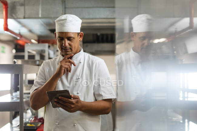 Porträt eines männlichen Profikochs mit gemischter Rasse, der auf Tabletten blickt. Arbeit in einer belebten Restaurantküche. — Stockfoto