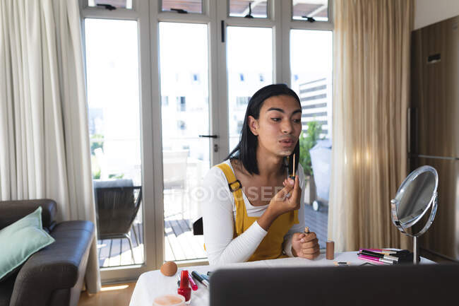 Mixed race transgender woman making vlog using laptop putting on makeup. staying at home in isolation during quarantine lockdown. — Stock Photo