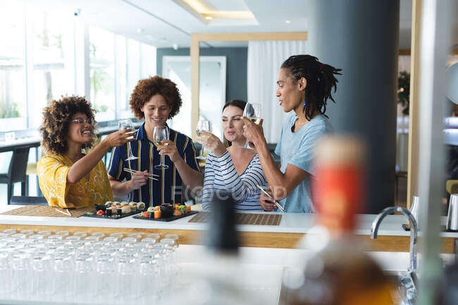 Diverso grupo de colegas masculinos y femeninos levantando copas de vino en el bar. amigos socializando y bebiendo en el bar. - foto de stock
