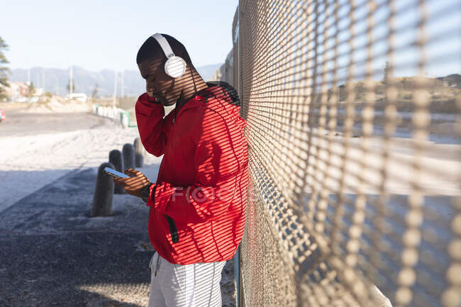 African american man exercising outdoors, wearing headphones, using smartphone, listening music. healthy outdoor lifestyle fitness training. — Stock Photo