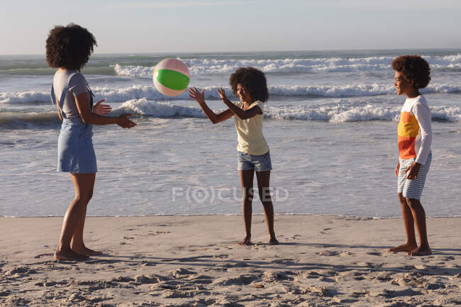 Afrikanisch-amerikanische Mutter und zwei Kinder spielen mit einem Ball am Strand. Familienfreizeit im Freien am Meer. — Stockfoto