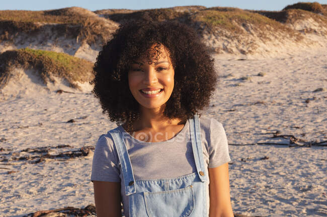 Портрет афро-американської жінки, яка дивиться на камеру і посміхається на пляжі. Здоровий вільний час на відкритому повітрі біля моря. — стокове фото