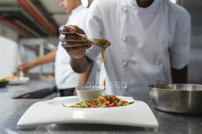 Sección media del plato final del chef profesional de raza mixta antes de servir. trabajando en una cocina ajetreada. - foto de stock