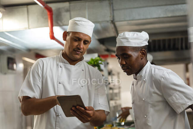 Portrait de divers chefs professionnels de race masculine discutant sur tablette. travailler dans une cuisine de restaurant occupée. — Photo de stock