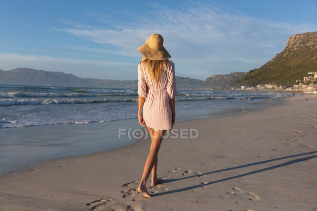 Caucasian woman wearing beach cover up and hat having fun walking at the beach. healthy outdoor leisure time by the sea. — Fotografia de Stock