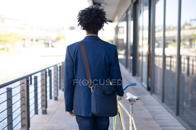 Smartly dressed mixed race male wheeling bicycle in the street. green urban lifestyle, out and about in the city. — Stock Photo