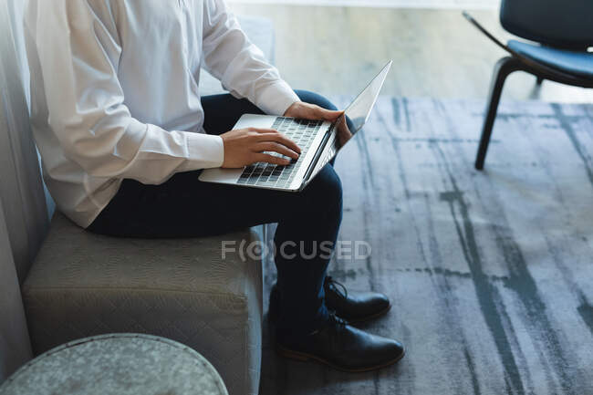 Sezione centrale di uomo d'affari seduto nella hall dell'hotel a lavorare su laptop. viaggi d'affari settore alberghiero. — Foto stock