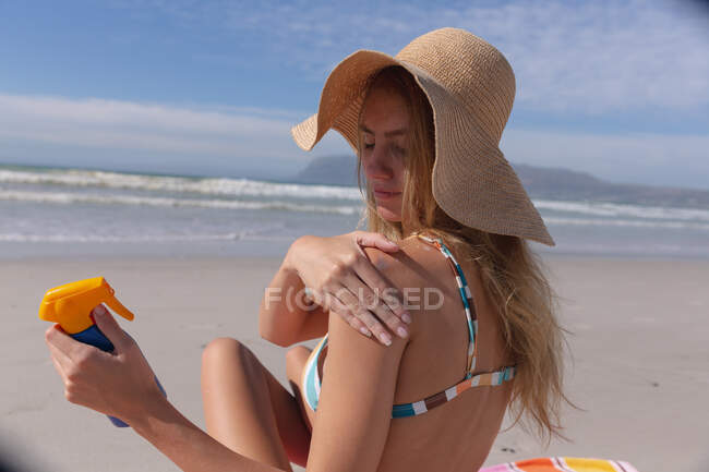 Жінка в бікіні сидить на рушнику і кладе сонцезахисний крем на пляж. Здоровий вільний час на відкритому повітрі біля моря. — стокове фото