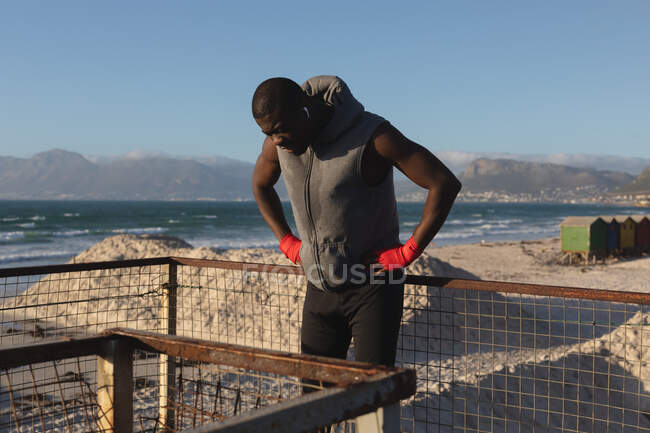 African american man exercising outdoors, resting on pier at sunset. healthy outdoor lifestyle fitness training. — Stock Photo