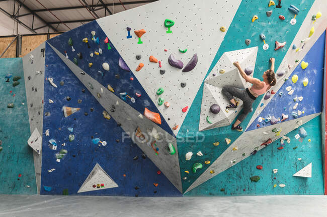 Mulher branca a subir uma parede no ginásio de escalada interior. fitness e tempo de lazer no ginásio. — Fotografia de Stock