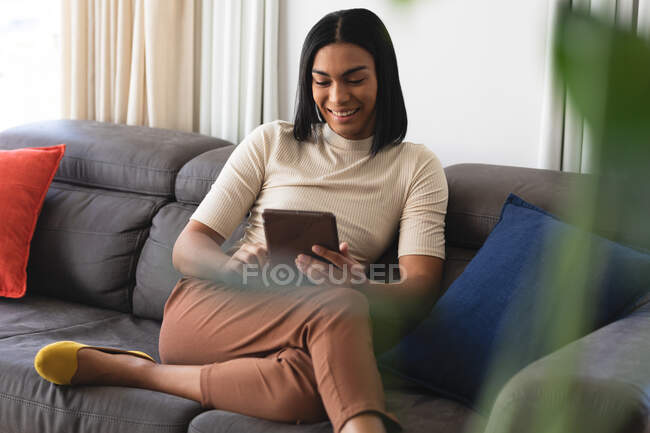 Felice razza mista transgender donna rilassante in soggiorno seduto sul divano con tablet. stare a casa in isolamento durante la quarantena. — Foto stock