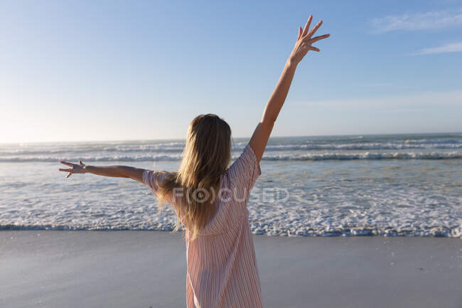 Kaukasische Frau in Strandkleidung, die die Hände am Strand hebt. gesunde Freizeit im Freien am Meer. — Stockfoto