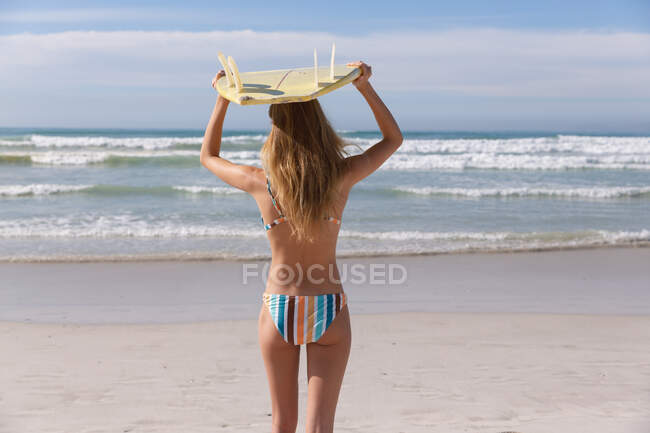 Caucasian woman wearing bikini carrying surfboard on her head at the beach. healthy outdoor leisure time by the sea. — Stock Photo