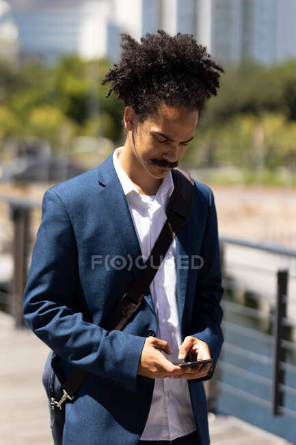 Hombre de raza mixta inteligentemente vestido con bigote caminando por la calle usando un teléfono inteligente. nómada digital, fuera y alrededor de la ciudad. - foto de stock