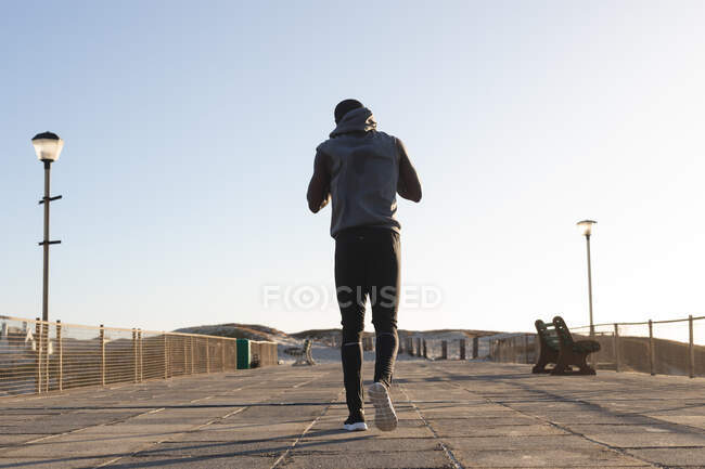 Vue arrière de l'homme afro-américain faisant de l'exercice en plein air marchant sur le pont au coucher du soleil. mode de vie sain en plein air entraînement fitness. — Photo de stock