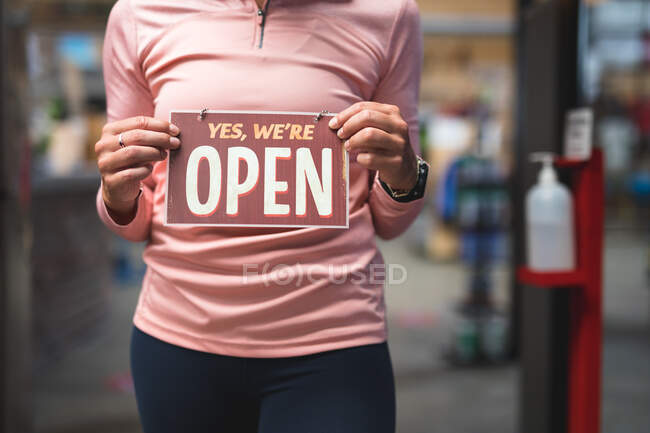 Midsection of caucasian woman holding open sign in corridor at gym. fitness and leisure time at gym during coronavirus covid 19 pandemic. — Stock Photo
