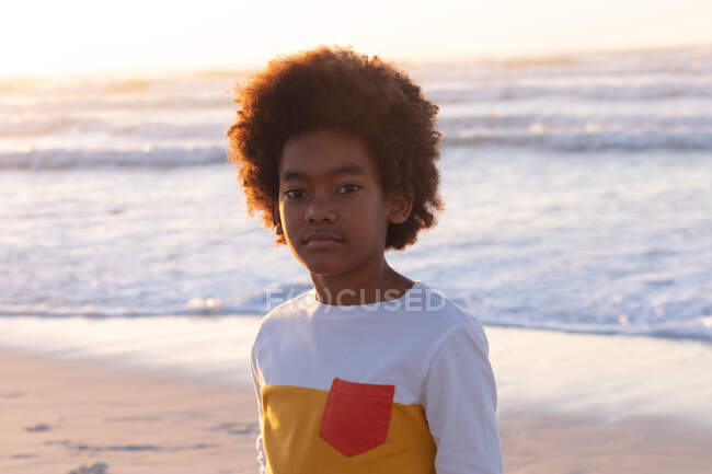 Portrait of african american boy looking at camera and smiling at the beach. healthy outdoor leisure time by the sea. - foto de stock