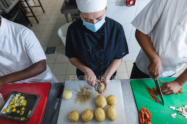 Diverse race male and female professional chefs preparing vegetables wearing face masks. working in a busy restaurant kitchen during coronavirus covid 19 pandemic. — Stock Photo