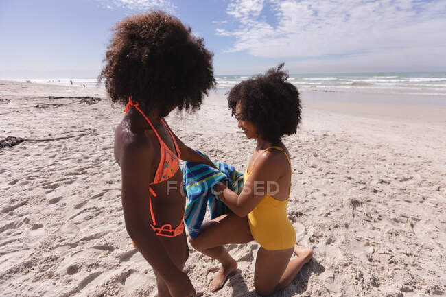 African american mother and daughter wiping with a towel at the beach smiling. healthy outdoor leisure time by the sea. — Fotografia de Stock