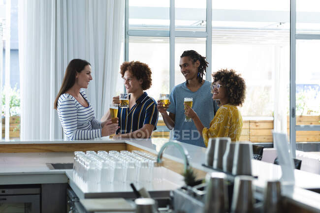 Diverso grupo de colegas masculinos y femeninos riendo y tomando cerveza en el bar. amigos socializando y bebiendo en el bar. - foto de stock