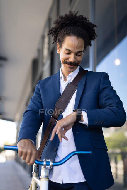 Elegantemente vestito misto corsa maschile ruote bicicletta guardando orologio in strada. stile di vita urbano verde, in giro per la città. — Foto stock