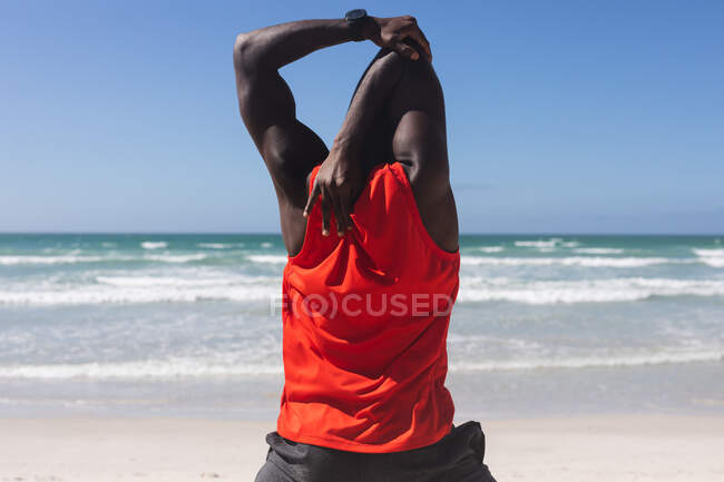Back view of african american man exercising, stretching on beach. healthy outdoor lifestyle fitness training. — Stock Photo