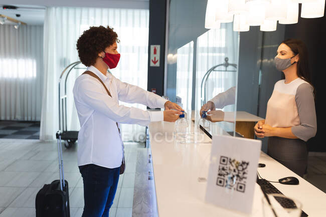 Diverso empresário usando máscara facial desinfetando as mãos conversando com recepcionista no hotel. hotel de viagens de negócios durante coronavírus covid 19 pandemia. — Fotografia de Stock