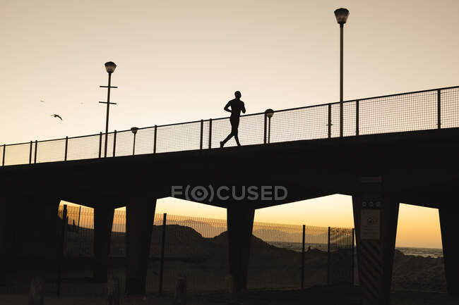 Африканский американец тренируется на открытом воздухе, бегая по мосту на закате. фитнес-тренировки. — стоковое фото