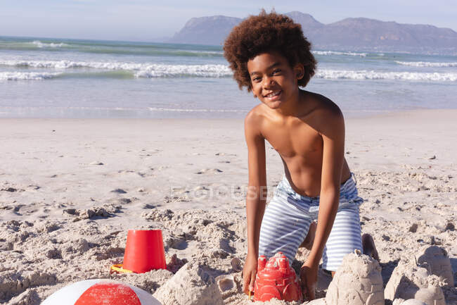 African american boy having fun playing with sand at the beach. family outdoor leisure time by the sea. — Stock Photo