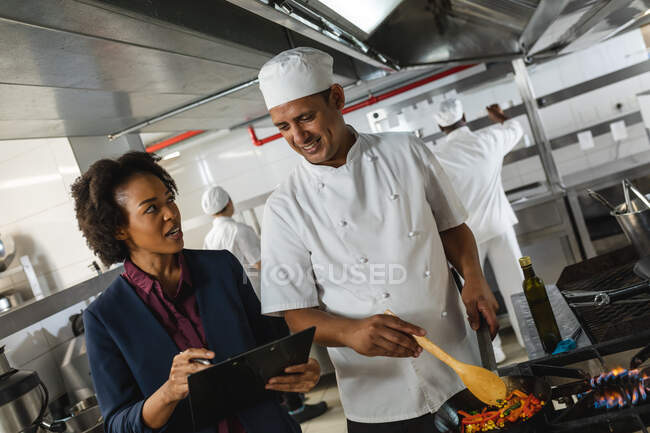 Corrida diversa gerente de cozinha do sexo feminino discutindo com chef profissional sobre tablet. trabalhando em uma cozinha restaurante ocupado. — Fotografia de Stock