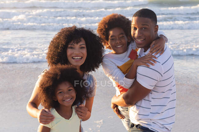 Portrait of smiling african american parents and two children embracing at the beach. family outdoor leisure time by the sea. — Foto stock