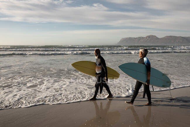 Senior african american couple carrying surf boards walking on the beach. travel vacation retirement lifestyle concept — Stock Photo