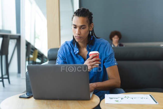 Retrato de homem de negócios de raça mista sentado no sofá usando laptop e tomando café. reunião informal na sala de negócios. — Fotografia de Stock