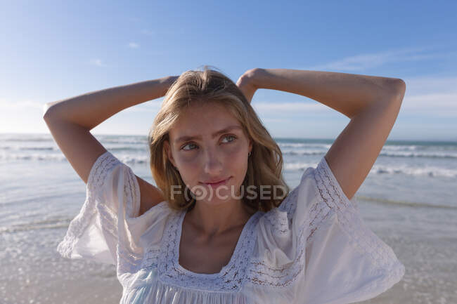 Усміхнена біла жінка стоїть з руками за головою на пляжі. здоровий відпочинок на відкритому повітрі біля моря . — стокове фото