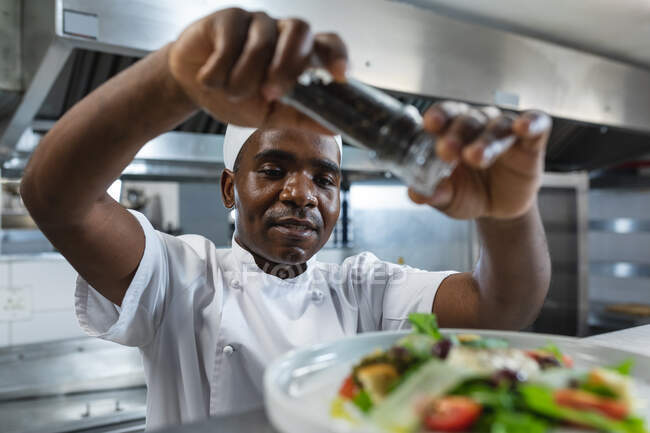 Glückliche afrikanisch-amerikanische Profi-Koch fertig Gericht vor dem Servieren. Arbeit in einer belebten Restaurantküche. — Stockfoto