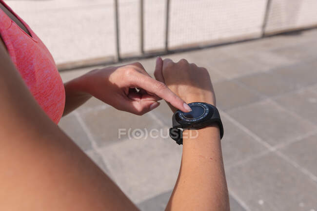 Mujer caucásica haciendo ejercicio usando su smartwatch en un paseo marítimo por la playa. Tiempo de ocio al aire libre saludable junto al mar. - foto de stock