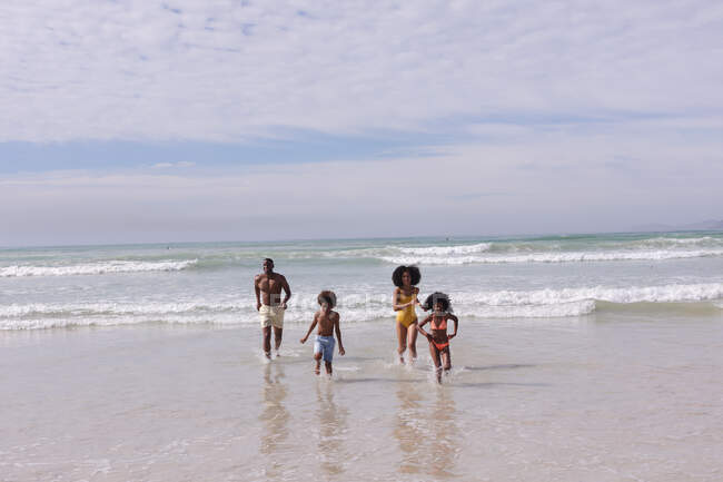 Африканські американські батьки і двоє дітей біжать на пляжі посміхаючись. сім'я на відкритому повітрі відпочиває біля моря. — стокове фото