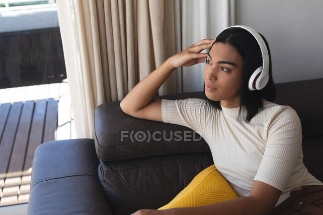 Happy mixed race transgender woman relaxing in living room sitting on couch with headphones. staying at home in isolation during quarantine lockdown. — Stock Photo