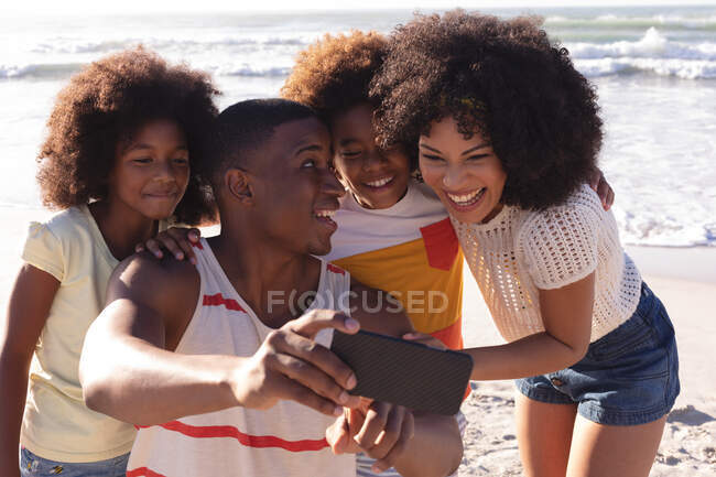 African american parents and two children taking a selfie with smartphone at the beach smiling. family outdoor leisure time by the sea. - foto de stock