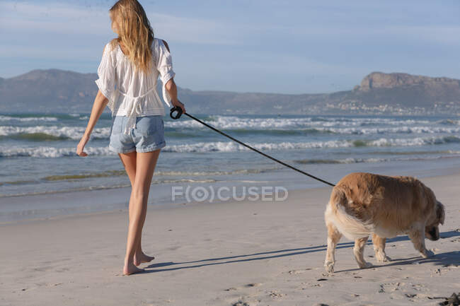 Donna caucasica che porta a spasso un cane sulla spiaggia. sano tempo libero all'aperto in riva al mare. — Foto stock