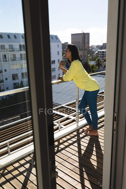 Transgender-Frau mit gemischter Rasse steht auf sonniger Dachterrasse und trinkt Kaffee. Isolationshaft während der Quarantäne. — Stockfoto