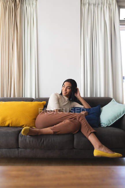 Feliz mestiço transgênero mulher relaxante na sala de estar sentado no sofá sorrindo. ficar em casa em isolamento durante o confinamento de quarentena. — Fotografia de Stock