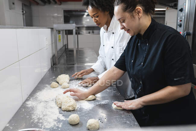 Mixed race professional chefs preapring dough on countertop covered with flour. working in a busy restaurant kitchen. — Stock Photo