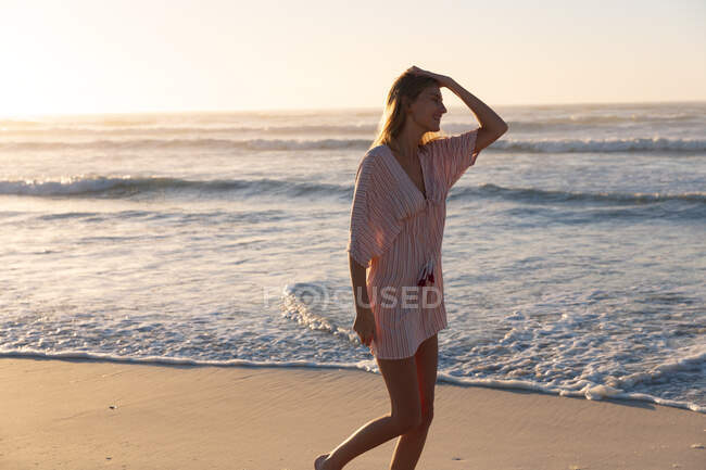 Hermosa mujer caucásica caminando y disfrutando en la playa al atardecer. verano playa vacaciones concepto. - foto de stock