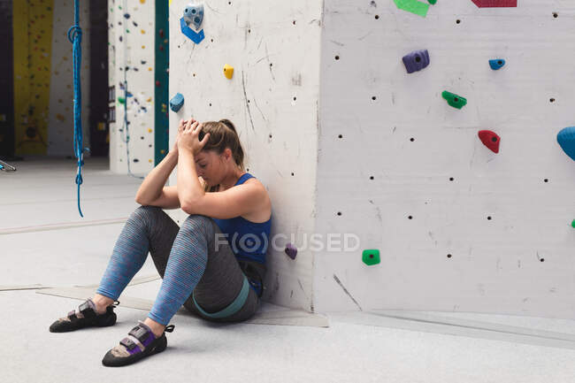 Mujer caucásica descansando apoyada en la pared de escalada en el muro de escalada interior. fitness y tiempo libre. - foto de stock