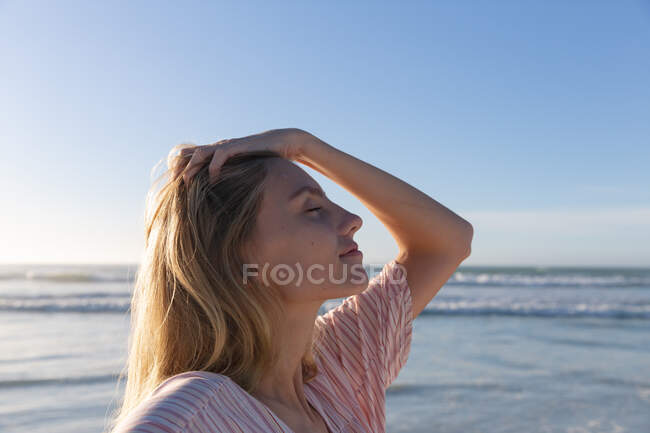 Kaukasische Frau in Strandkleidung, die ihre Haare am Strand berührt. gesunde Freizeit im Freien am Meer. — Stockfoto